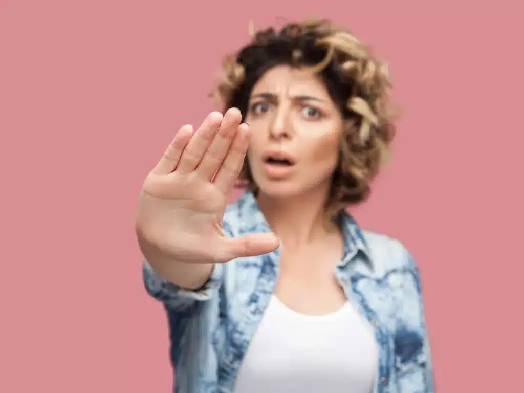 Contre-indications de l'injection d'acide hyaluronique : femme aux cheveux bouclés tendant la main pour dire stop, sur fond rose