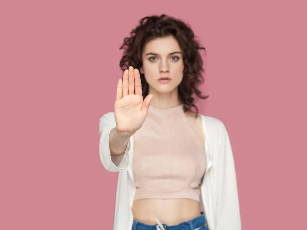 Contre-indications de l'injection d'acide hyaluronique : femme aux cheveux bouclés levant la main pour dire stop, sur fond rose