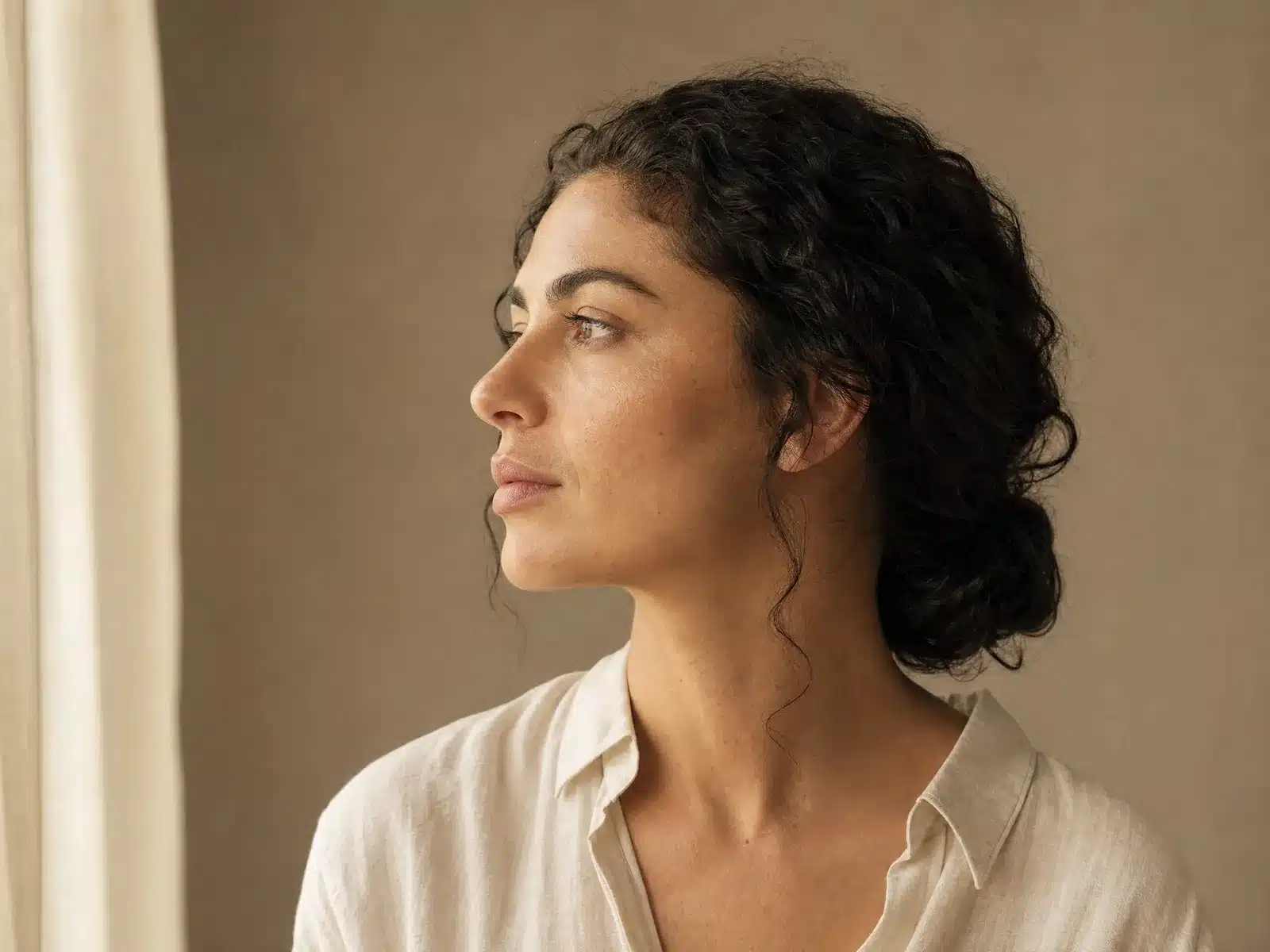 Injection d'acide hyaluronique au rendu naturel : profil d'une femme aux cheveux bruns bouclés, lèvres et ligne du menton harmonieuses