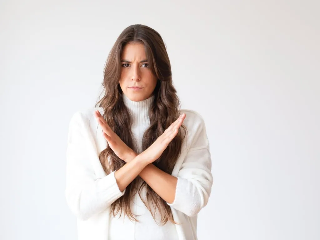 Contre-indications de l'injection d'acide hyaluronique : femme en pull blanc croisant les bras pour dire non