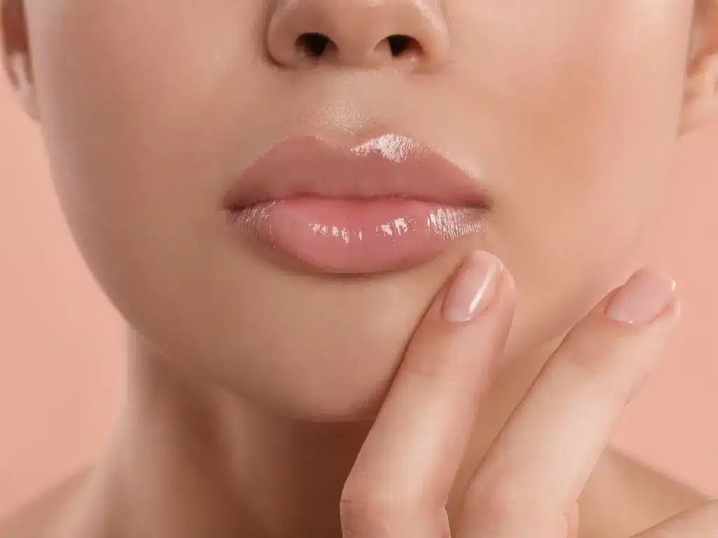 Injection d'acide hyaluronique des lèvres : bas du visage d'une femme aux lèvres pulpeuses, doigt posé sous la lèvre inférieure