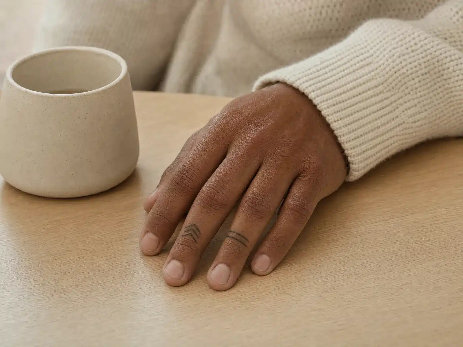 Détatouage laser à Bordeaux : main d'homme posée sur une table en chêne clair, petits tatouages géométriques noirs sur les doigts