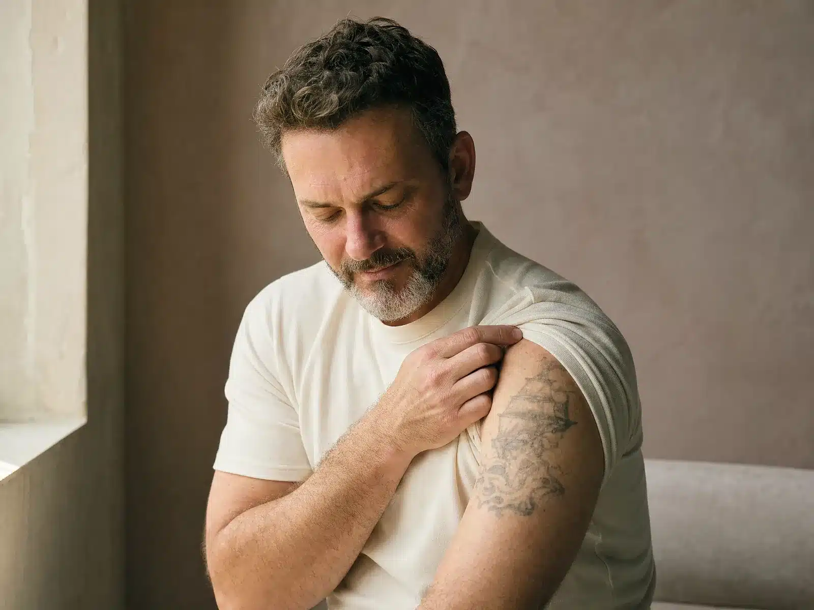Détatouage laser à Paris : homme à la barbe poivre et sel regardant un ancien tatouage noir et gris sur le haut de son bras