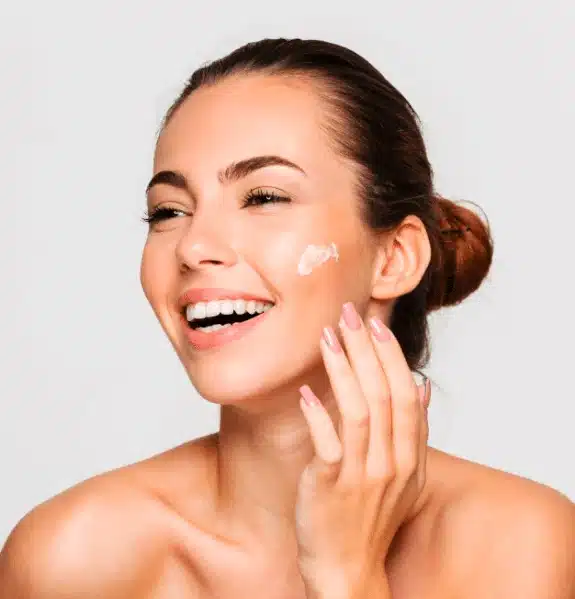 Femme souriante qui applique une crème sur sa joue