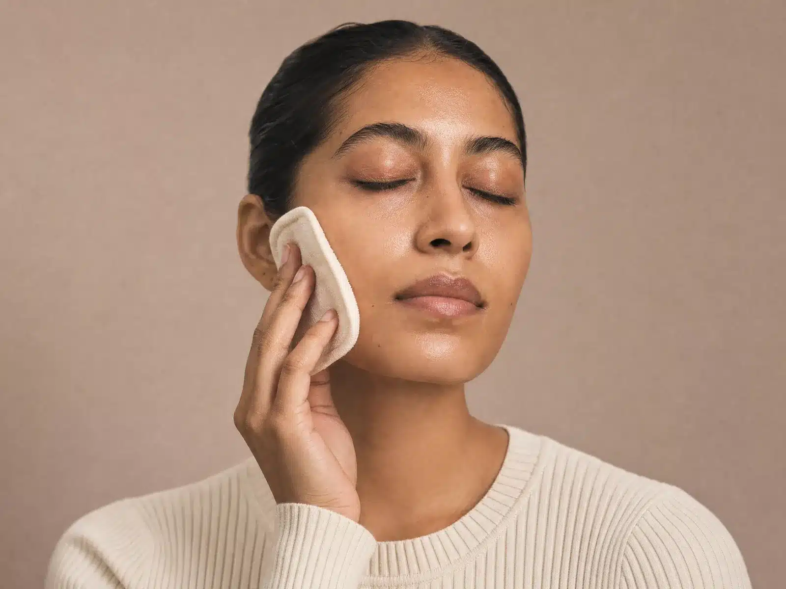 Préparation de la peau avant un peeling à Lyon : femme aux yeux fermés tenant un coton ivoire contre sa joue