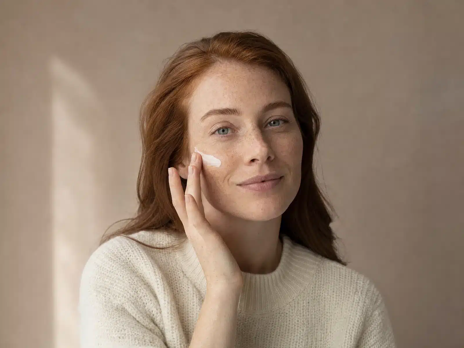 Soin après un peeling à Nice : femme aux taches de rousseur appliquant une crème légère sur la pommette du bout des doigts