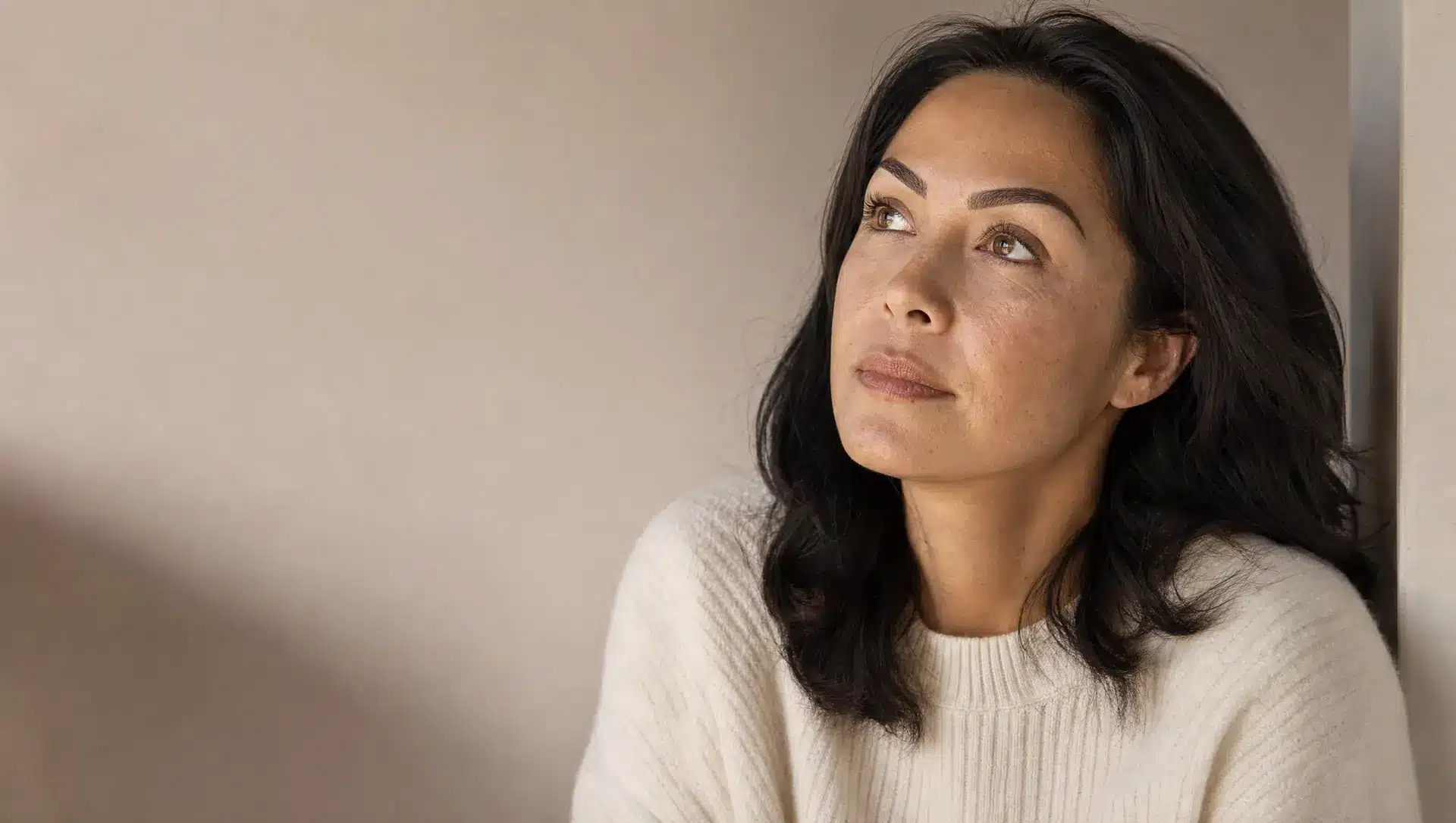 Gros plan sur une femme à la peau beige chaud, aux sourcils semi-permanents foncés et trop marqués, les yeux ouverts levés vers le haut