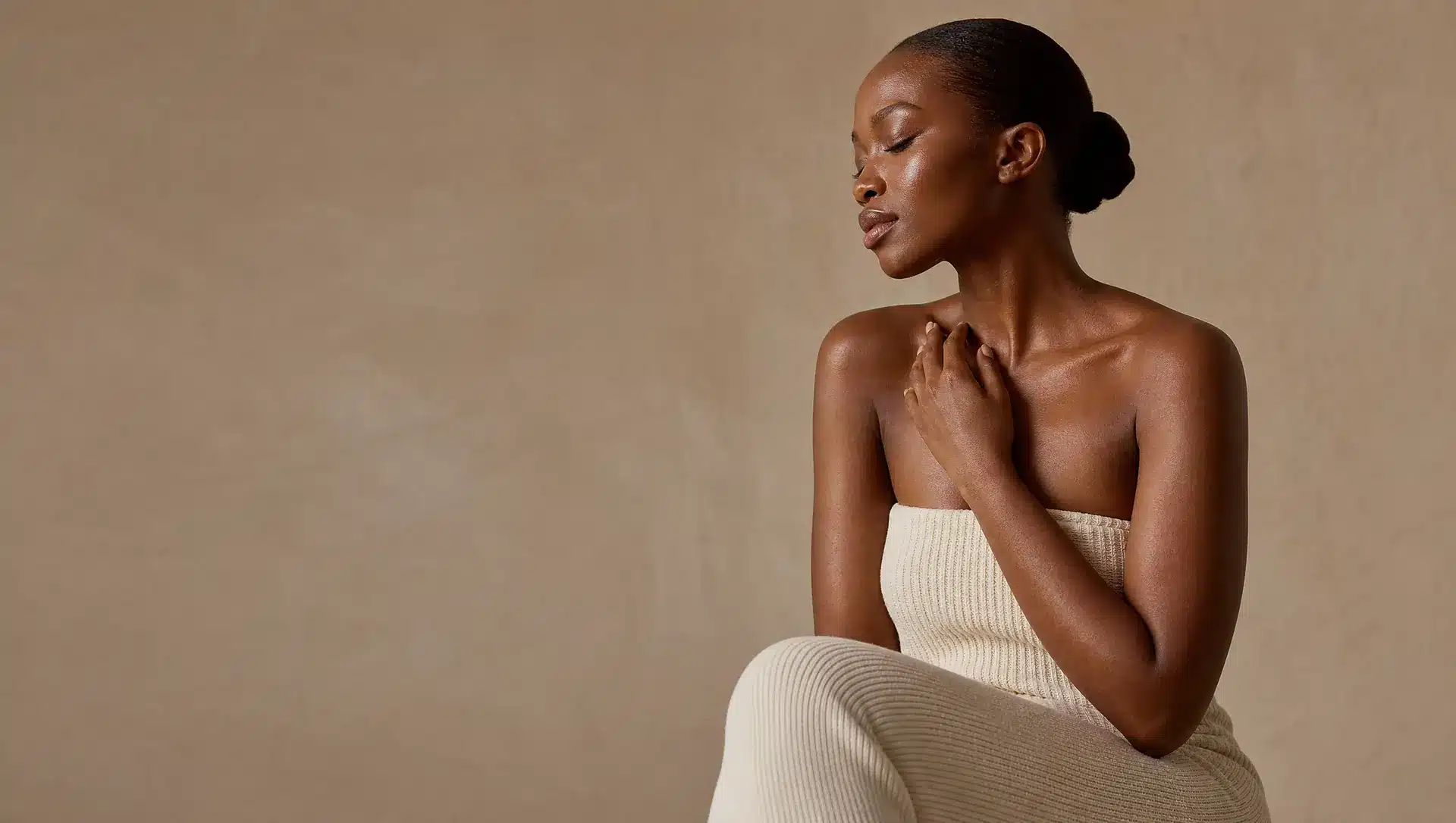 Femme à la peau noire en robe ivoire, une main posée sur la clavicule