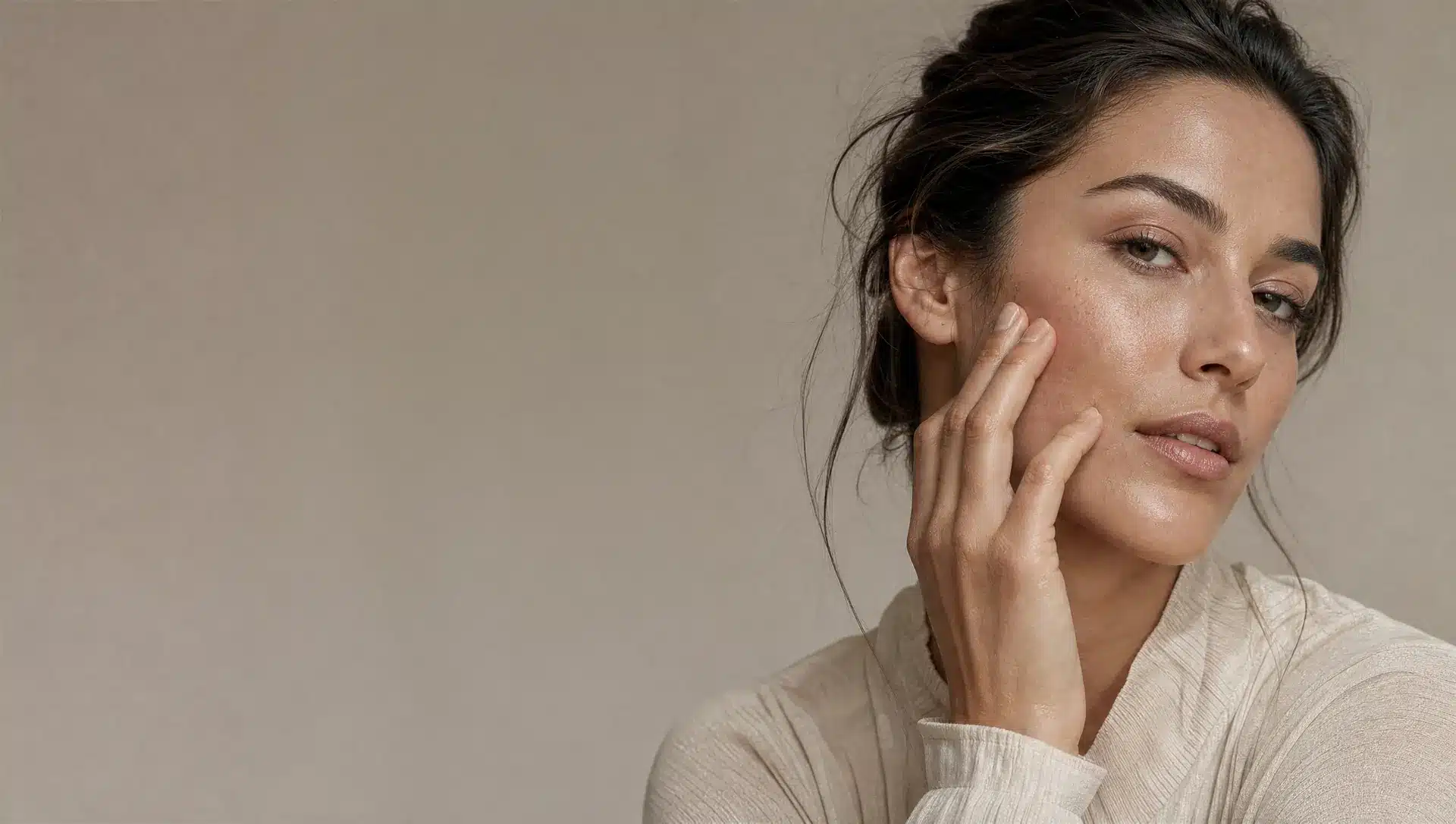 Joue d'une femme à la peau beige clair, repulpée, hydratée et lumineuse, le bout des doigts posé sur la pommette