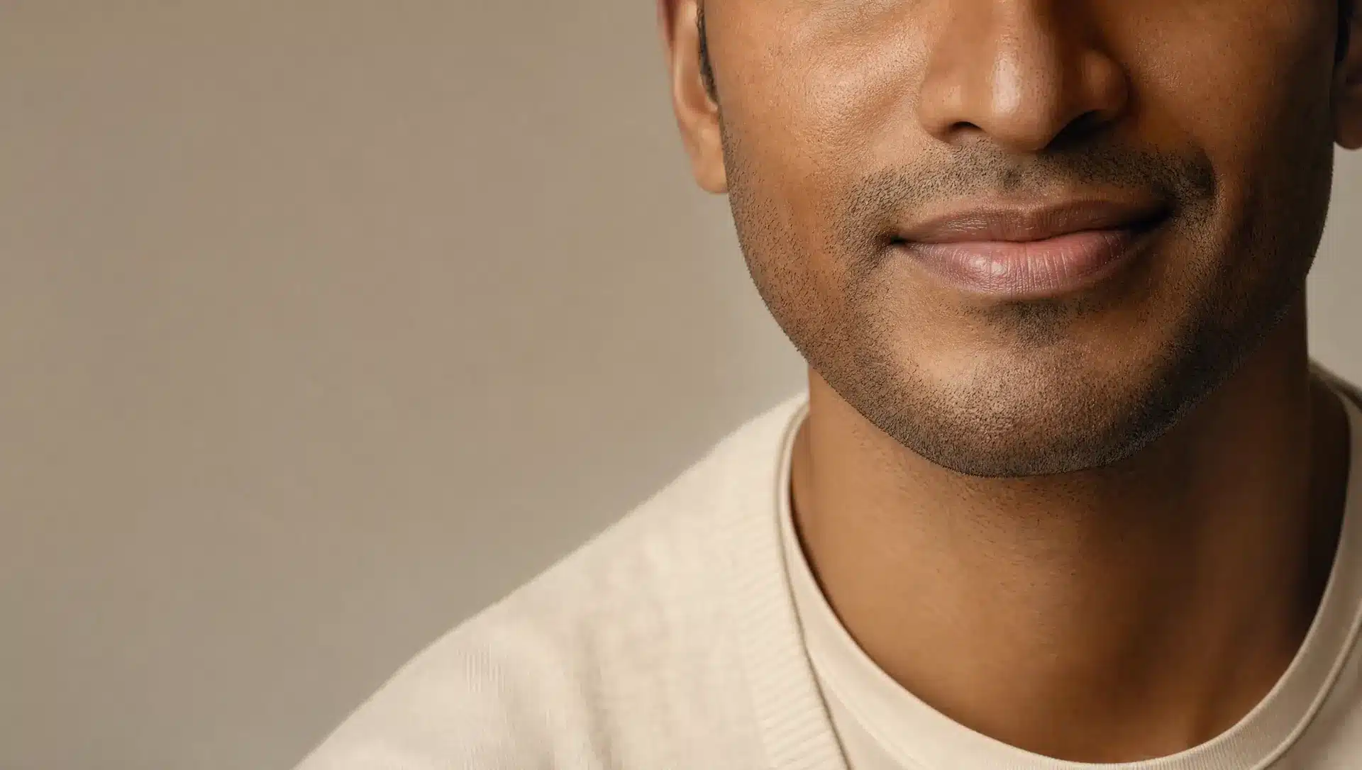Gros plan sur les lèvres et le menton d'un homme à la peau brun moyen, à la teinte de lèvres naturelle et homogène, esquissant un léger sourire
