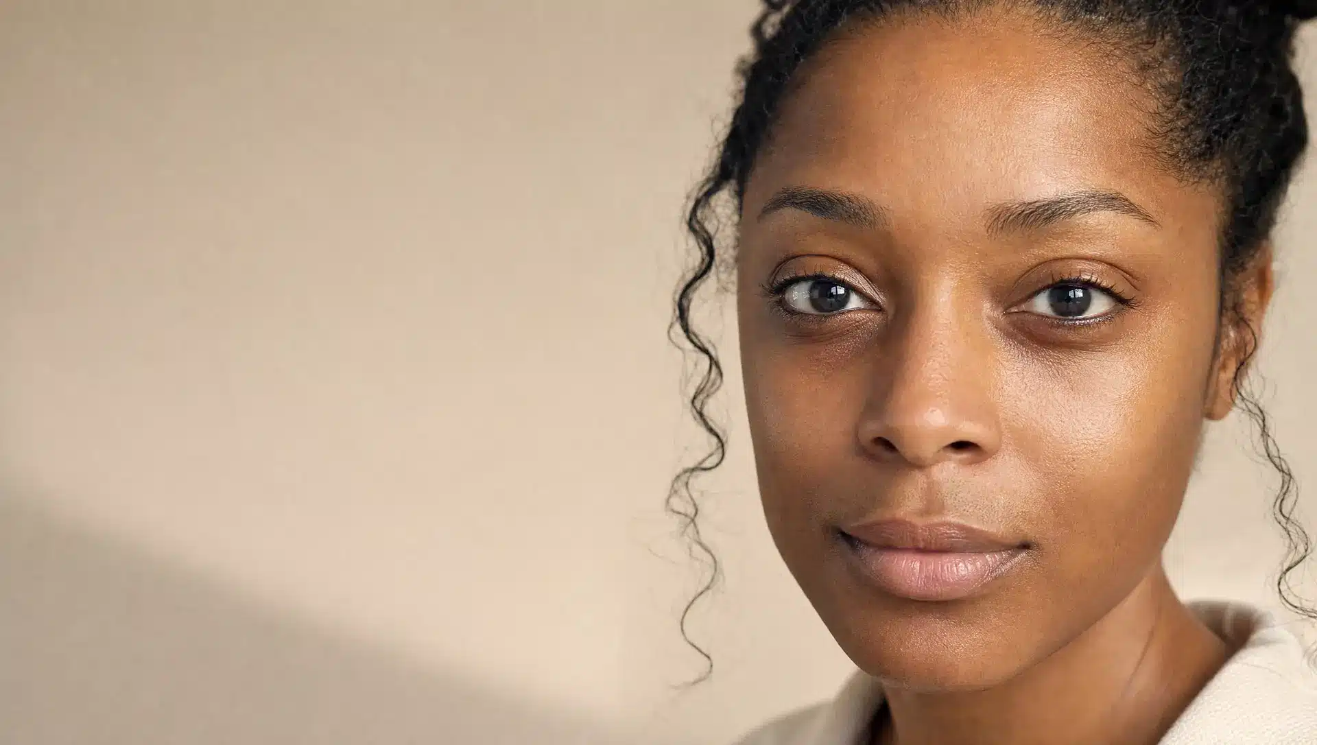 Portrait en gros plan d'une femme à la peau brun foncé, cernes légèrement plus sombres, yeux ouverts et expression calme