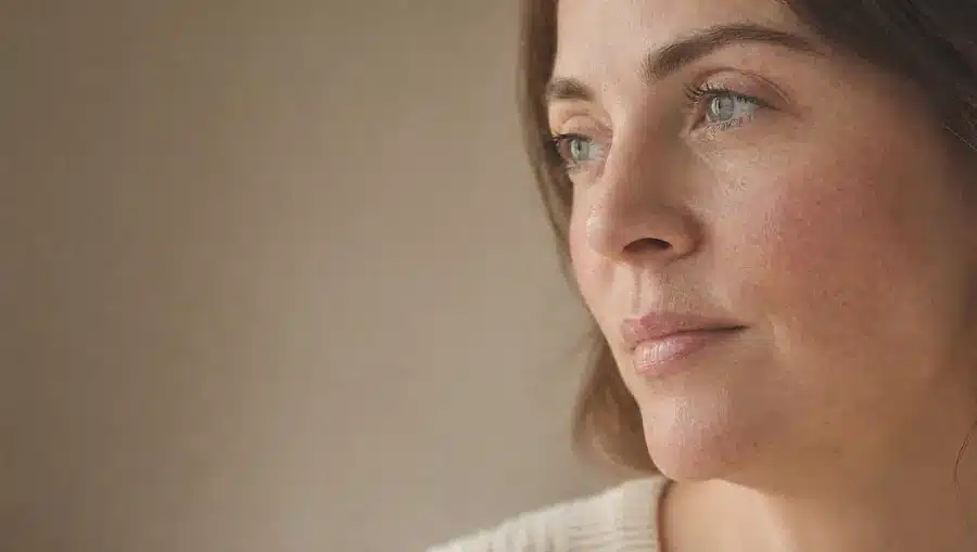 Gros plan sur la joue et le nez d'une femme à la peau claire parsemée de taches de rousseur, aux fins capillaires rouges visibles, en lumière naturelle
