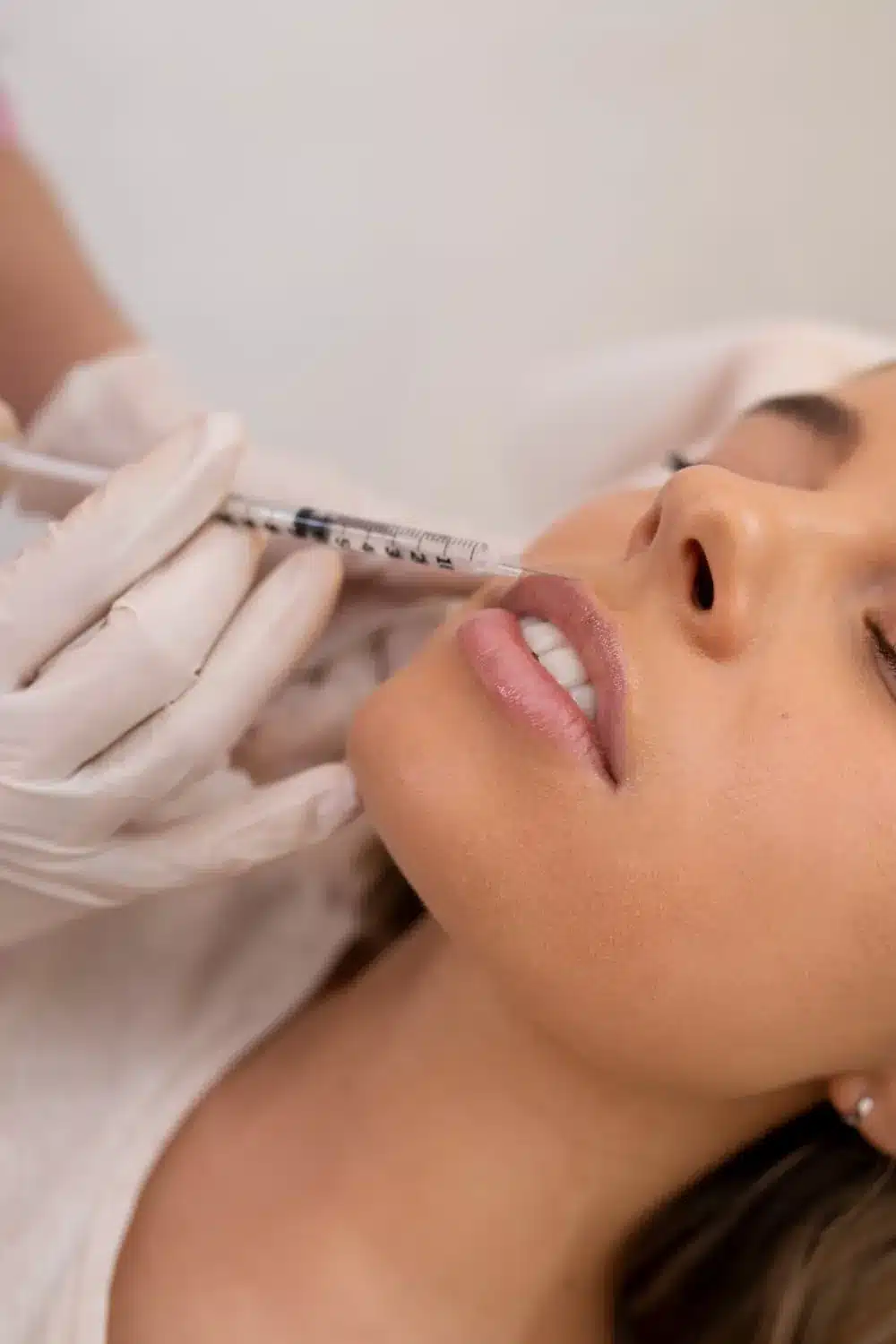 Injection dans la lèvre supérieure d'une patiente allongée, seringue tenue par des mains gantées
